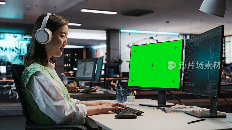 亚洲女性游戏程序员在游戏设计工作室办公室用绿屏Chromakey在台式电脑上编程。专注女性为全新沉浸式3D RPG电子游戏设计游戏玩法
